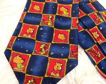 Könnte beinhalten: Eine blaue Krawatte mit einem sich wiederholenden Muster von Winnie Puuh und Tigger in roten Rahmen. Die Krawatte hat einen marineblauen Hintergrund mit einem Gittermuster und goldenen Rändern. Die Krawatte ist aus glänzendem Material.