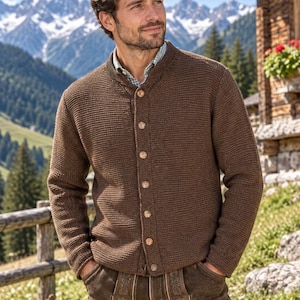 May include: A brown knit cardigan featuring a round neckline and a front button closure with light-coloured buttons. The garment is worn over a light-coloured checkered shirt and paired with dark brown leather trousers featuring decorative embroidery.