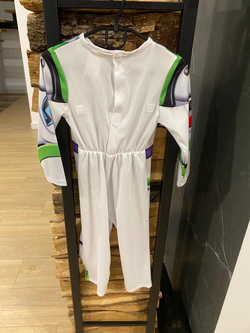 May include: White Buzz Lightyear costume with green, black, and purple accents. The costume features long sleeves and a jumpsuit design, with details mimicking the character's space suit. The costume is hanging on a black hanger.