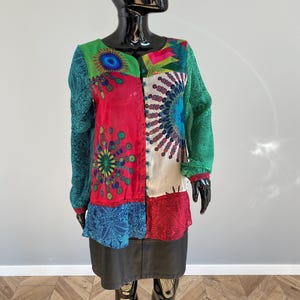 Könnte beinhalten: Eine langärmelige Bluse mit Patchwork-Design in leuchtenden Farben wie Rot, Grün, Blau und Weiß. Das Kleidungsstück zeigt komplexe kreisförmige Mandala-Muster, Paisley-Motive und eine durchgehende Knopfleiste auf der Vorderseite.
