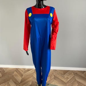 May include: A long-sleeved jumpsuit featuring a vibrant red shirt top integrated with blue overalls. The design includes two large, bright yellow circular buttons positioned at the top of the blue overall straps on the chest area.