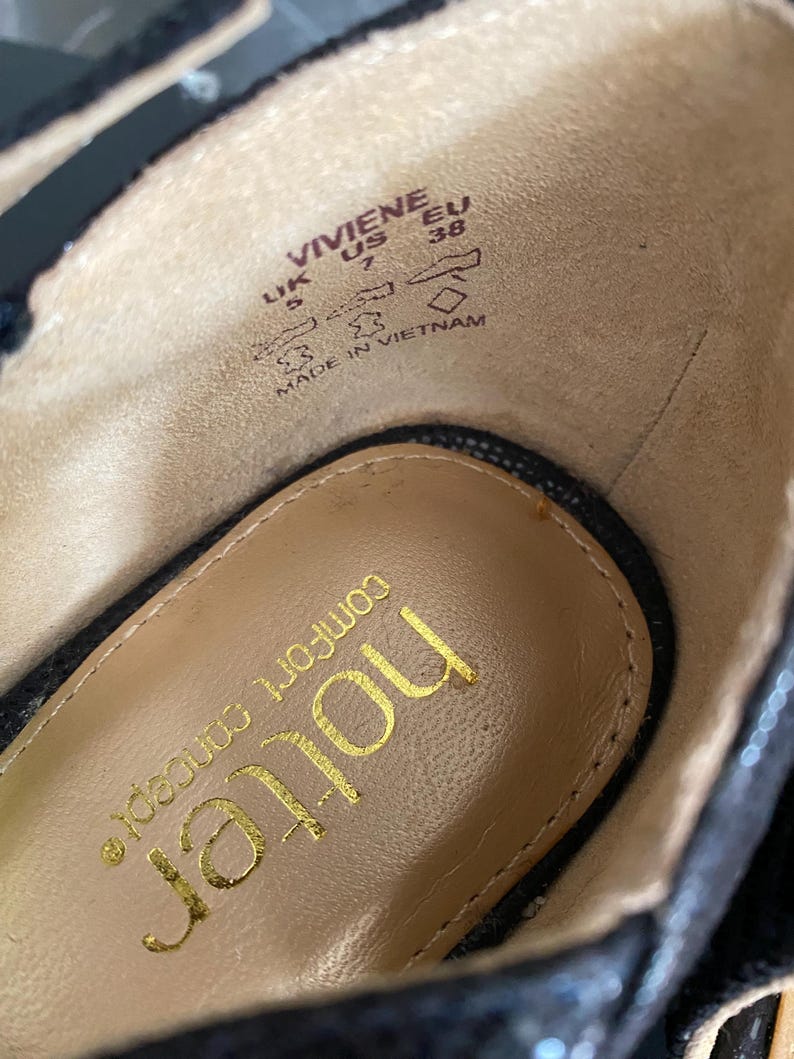May include: The interior of a black shoe with a tan insole featuring the gold text 'hotter' and 'comfort concept'. The side wall displays the text 'VIVIENE', 'UK 5', 'US 7', 'EU 38', and 'MADE IN VIETNAM' along with icons representing shoe construction.