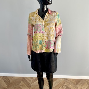 May include: A patterned button-down shirt with long sleeves, featuring a mix of floral and geometric designs in pink, yellow, and green. The shirt is paired with a black leather skirt. The outfit is displayed on a black mannequin.