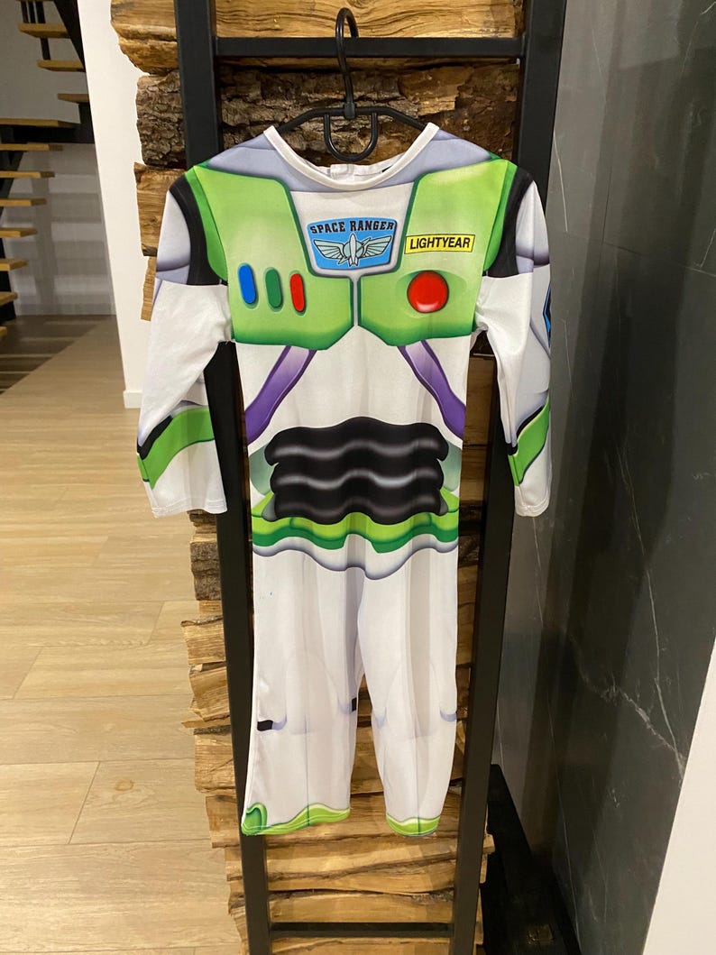 May include: A Buzz Lightyear costume, featuring a white jumpsuit with green and purple accents. The chest area has a green panel with the words "SPACE RANGER" and "LIGHTYEAR". The costume has long sleeves and is hanging on a black hanger.