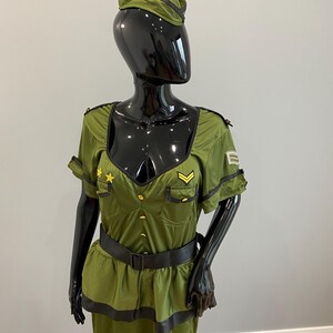 May include: Olive green military-style costume with a matching hat. The outfit features a fitted bodice with gold buttons, a black belt, and a skirt. The hat has a black trim. The costume is displayed on a black mannequin.