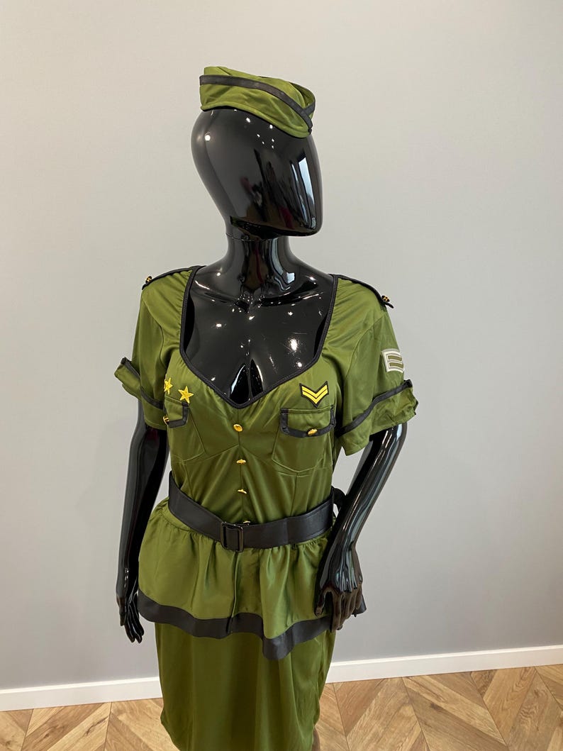 May include: Olive green military-style costume with a matching hat. The outfit features a fitted bodice with gold buttons, a black belt, and a skirt. The hat has a black trim. The costume is displayed on a black mannequin.