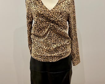 Op de afbeelding: Een mannequin toont een top met lange mouwen en een zwarte rok. De top heeft een V-hals en een bruin-zwarte luipaardprint. De rok is effen zwart. De outfit wordt gepresenteerd tegen een lichte achtergrond.