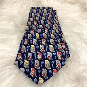 Può includere: Cravatta blu navy con un motivo paisley ripetuto in rosso, giallo e grigio. La cravatta presenta piccoli accenti floreali blu. La cravatta è piegata e presentata su una superficie bianca e soffice.