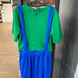May include: A green and blue costume dress hanging on a black hanger. The top is green with blue suspenders, and the skirt is blue. The dress is made of a soft, lightweight fabric. The dress is designed to be worn as a costume.