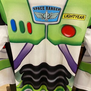 May include: A Buzz Lightyear costume featuring a white and green design with the words "SPACE RANGER" and "LIGHTYEAR". The costume has a series of colored buttons and a red circular button on the chest.