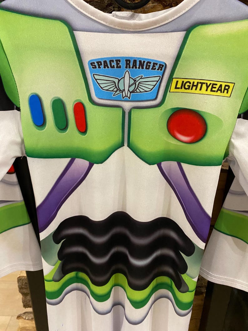 May include: A Buzz Lightyear costume featuring a white and green design with the words "SPACE RANGER" and "LIGHTYEAR". The costume has a series of colored buttons and a red circular button on the chest.
