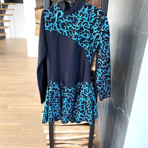 May include: A black long-sleeved dress with a high collar and a flared skirt. The dress features a striking design of swirling blue patterns on the sleeves, bodice, and skirt, creating a bold contrast against the black fabric. The dress is hanging on a black hanger.
