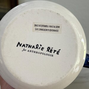 K&ouml;nnte beinhalten: Wei&szlig;er Keramikkrugboden mit dem Text "Nathalie Lete for Anthropologie" in schwarzer Schrift. Der Boden des Krugs hat einen Aufkleber mit der Aufschrift "Dishwasher & Microwave Safe Made in China/Fabriqu&eacute; en Chine."