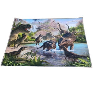 K&ouml;nnte beinhalten: Ein farbenfroher Teppich mit Dinosaurier-Motiv, der verschiedene Dinosaurier in einer pr&auml;historischen Landschaft zeigt. Der Teppich zeigt eine Flussszene mit mehreren Dinosauriern, darunter Tyrannosaurus Rex und Triceratops, vor dem Hintergrund von Bergen und Wasserf&auml;llen.