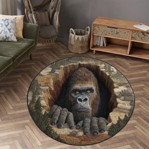 Könnte beinhalten: Runder Teppich mit einer detaillierten Illustration eines Gorillas, der aus einer felsigen Öffnung auftaucht. Der Teppich hat einen schwarzen Rand und eine Waldszene um den Gorilla. Der Gorilla hat gelbe Augen.