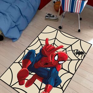 May include: A rectangular rug featuring a Spider-Man illustration. The superhero is depicted in his classic red and blue suit, posed against a cream-colored background with a black spiderweb design. A black spider silhouette is in the corner.