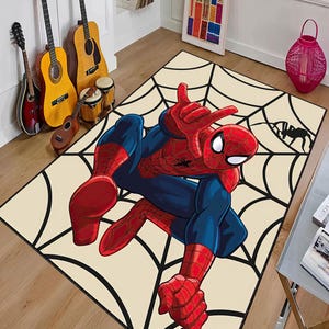 May include: A rectangular rug featuring a large illustration of Spider-Man in a dynamic pose, set against a cream-colored background with a black spiderweb design. The superhero is depicted in his classic red and blue suit.