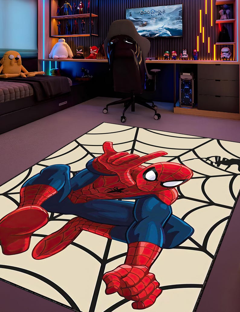 May include: A rectangular rug featuring a Spider-Man illustration in red and blue, posed on a cream-colored background with a black spiderweb design. The rug is in a room with a gaming setup and superhero figurines.