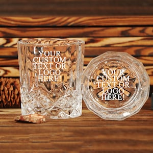 以下が含まれることがあります： 透明なファセット加工のグラスが2つ。1つは直立し、もう1つは横向きで、「YOUR CUSTOM TEXT OR LOGO HERE！」の文字が表示されています。背景は木製の表面です。