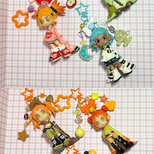 May include: A collection of colorful, stylized figurines with orange and blue hair, each adorned with unique accessories like stars, hearts, and bows. The figurines are arranged on a pink and white checkered surface.