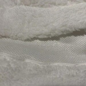 May include: Close-up of white fabric showing a contrast of textures. The image features a fluffy, plush material alongside a smooth, woven fabric. The textures create a layered effect, with the fluffy material on top.