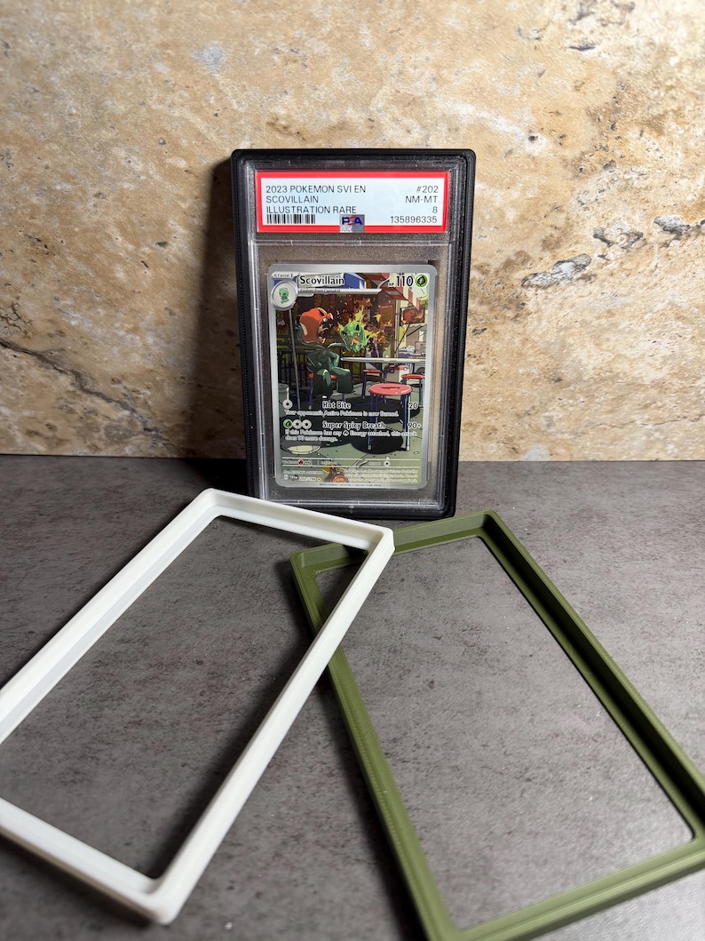Op de afbeelding: Een beoordeelde Pok&eacute;mon-kaart in een zwarte hoes, met een Scovillain-illustratie. De kaart is gelabeld met "2023 Pok&eacute;mon SV1EN" en "Illustration Rare". Twee rechthoekige frames, &eacute;&eacute;n wit en &eacute;&eacute;n olijfgroen, staan op de voorgrond.