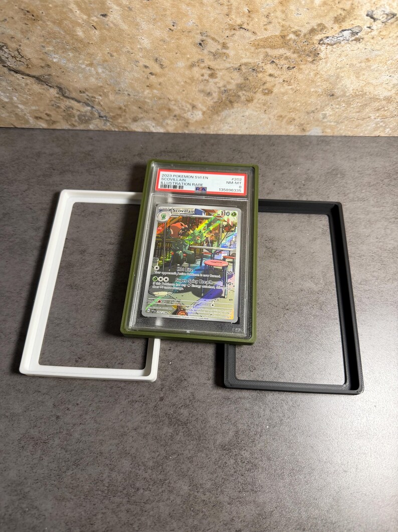 Op de afbeelding: Een beoordeelde Pok&eacute;mon-verzamelkaart in een groene houder, met de tekst "2023 Pokemon SWSH Scovillain Illustration Rare". De kaart wordt gepresenteerd met witte en zwarte beschermende frames.