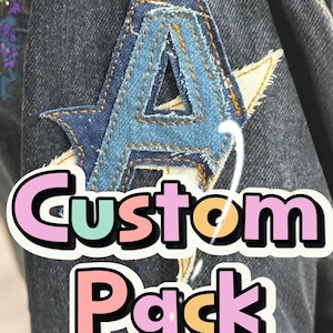 May include: A denim patch in the shape of the letter "A" with a star-like design, stitched onto a dark denim jacket. The patch is made of different shades of blue denim. The words "Custom Pack" are written in a colorful font.