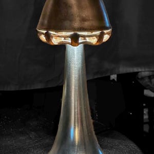 May include: A unique lamp with a metallic silver base and a brown, bell-shaped shade. The shade has a textured surface and a decorative, openwork design around the bottom. The lamp is illuminated from within, creating a warm glow. The text "WOLFOX Studios" is at the top.