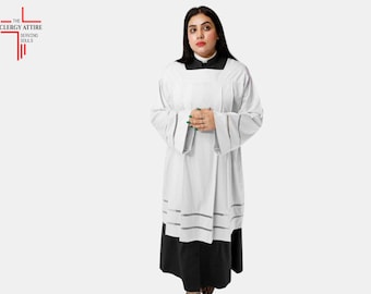 May include: A white clergy alb with a black skirt. The alb features a square black collar and wide sleeves. The garment has decorative gray stripes near the hem. The logo "THE CLERGY ATTIRE SERVING SOULS" is in the upper left corner.
