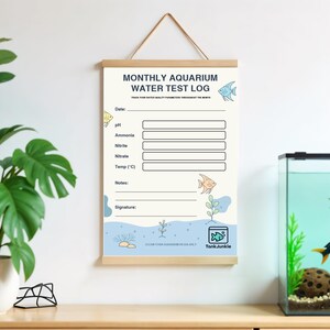 Puede incluir: Un colgante de pared beige con el texto "MONTHLY AQUARIUM WATER TEST LOG" y espacio para registrar los par&aacute;metros de calidad del agua. El registro presenta ilustraciones de peces y est&aacute; suspendido por una barra de madera y una cuerda.