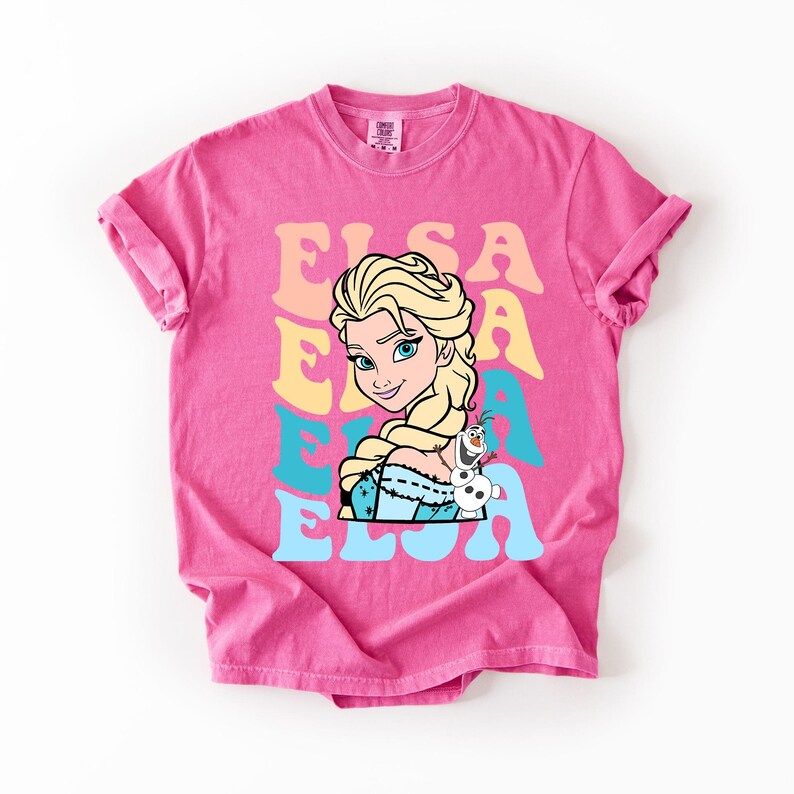 Puede incluir: Una camiseta rosa intenso con un gr&aacute;fico de Elsa de Frozen, con el nombre "ELSA" en una fuente retro. Elsa se representa con cabello rubio y un vestido azul, con Olaf el mu&ntilde;eco de nieve. Un dise&ntilde;o divertido y colorido.