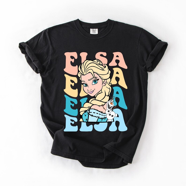 Puede incluir: Camiseta negra con un dise&ntilde;o retro de Elsa de Frozen. La palabra "ELSA" est&aacute; apilada en rosa, amarillo y azul. La imagen incluye a Elsa y Olaf el mu&ntilde;eco de nieve. El dise&ntilde;o es en tonos rosa, amarillo, azul y blanco.