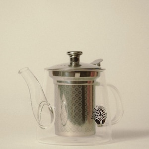 May include: A clear glass teapot with a stainless steel infuser and lid. The teapot has a curved spout and a handle. The words "Forest Friendly Tea" and a tree logo are printed on the side.