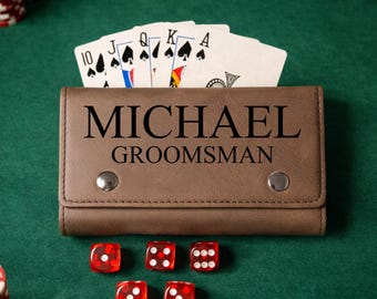 Könnte beinhalten: Ein braunes Lederportemonnaie mit dem Namen "MICHAEL" und dem Wort "GROOMSMAN" aufgedruckt. Pokerkarten sind hinter dem Portemonnaie aufgefächert. Fünf rote Würfel sind auf einer grünen Filzoberfläche verstreut. Pokerchips sind im Hintergrund zu sehen.