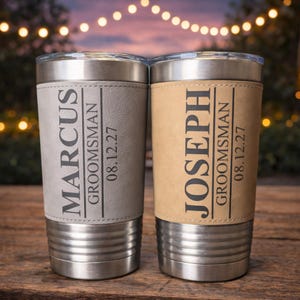 May include: Two stainless steel tumblers with personalized leather sleeves. One is gray and the other is tan. Each has a name, the word "Groomsman", and a date printed in black. The tumblers have a silver lid.