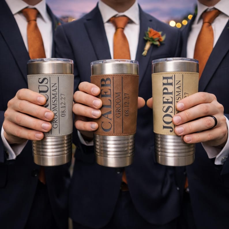 May include: Three stainless steel insulated tumblers with personalized leather sleeves. Each tumbler has a different name and role, with the date 08.12.27. The tumblers are held by people wearing navy suits and orange ties.