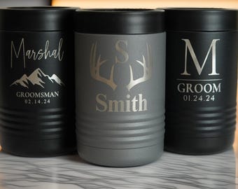 Könnte beinhalten: Drei isolierte Getränkehalter in Schwarz und Grau. Die schwarzen Halterungen tragen die Wörter "Marshal" und "Groomsman" mit einer Berg-Grafik sowie "Groom" mit dem Initial "M". Der graue Halter hat den Namen "Smith" und eine Hirschgeweih-Grafik.