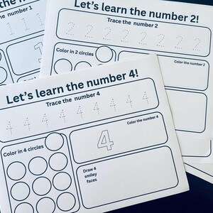 May include: White worksheets with the text "Let's learn the number" and numbers 1, 2, 4, and 8. Each worksheet includes tracing and coloring activities. The worksheets are stacked on a dark surface.