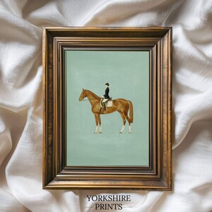 May include: A framed equestrian print featuring a rider on a brown horse against a light blue background. The print is in a gold-toned frame and includes the text "YORKSHIRE PRINTS" at the bottom.