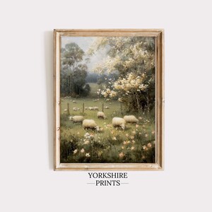 Op de afbeelding: Een ingelijst schilderij in vintage-stijl met schapen in een veld met bomen en bloemen. Het kunstwerk heeft een zacht kleurenpalet en is gevat in een rustieke houten lijst. De tekst "YORKSHIRE PRINTS" staat onderaan.