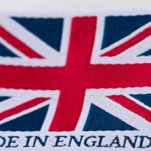 May include: A white fabric label featuring the Union Jack flag in red, white, and blue. The text "MADE IN ENGLAND" is printed in capital letters below the flag. The label has a stitched edge.