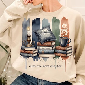 May include: Beige sweatshirt with a graphic of books, a candle, a pillow, and a coffee cup. The text "Just one more chapter" is below the graphic. The design has vertical color blocks in the background.
