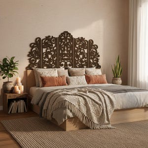 以下が含まれることがあります： 木製のベッドフレームと装飾的なヘッドボードを備えた寝室のシーン。ヘッドボードは、複雑な、濃い茶色の彫刻デザインです。ベッドは、ニュートラルな色合いの寝具、クッション、フリンジ付きの毛布で作られています。キャンドルと植物のある小さなサイドテーブルが見えます。