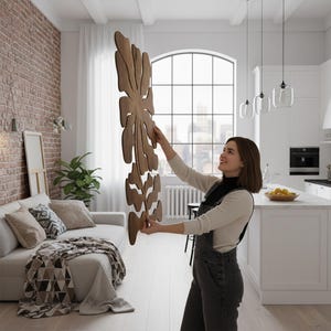 Peut inclure: Une grande d&eacute;coration murale en bois avec un motif de feuille est pr&eacute;sent&eacute;e dans un espace de vie lumineux et moderne. L'art est de couleur marron chaud et a une forme organique et fluide. La pi&egrave;ce comprend un mur de briques, un canap&eacute; blanc et de grandes fen&ecirc;tres.