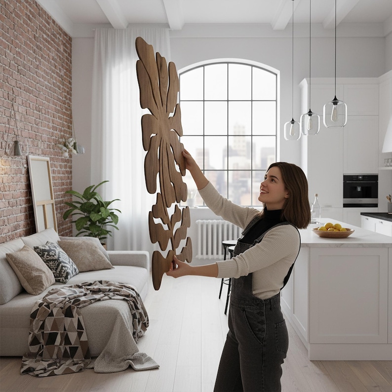 Peut inclure: Une grande d&eacute;coration murale en bois avec un motif de feuille est pr&eacute;sent&eacute;e dans un espace de vie lumineux et moderne. L'art est de couleur marron chaud et a une forme organique et fluide. La pi&egrave;ce comprend un mur de briques, un canap&eacute; blanc et de grandes fen&ecirc;tres.