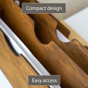 K&ouml;nnte beinhalten: Nahaufnahme eines Holzorganizers mit mehreren Schlitzen. Der Organizer besteht aus gebeiztem Holz und hat ein kompaktes Design. Der Text "Compact design" und "Easy access" sind auf dem Bild zu sehen.