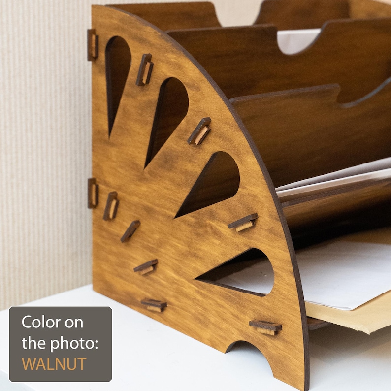 K&ouml;nnte beinhalten: Ein walnussfarbener Schreibtisch-Organizer aus Holz mit mehreren F&auml;chern. Der Organizer hat ein einzigartiges Design mit dekorativen Ausschnitten und ist f&uuml;r die Aufnahme von Papieren und Dokumenten konzipiert. Die Farbe auf dem Foto ist Walnuss.