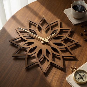 May include: A wooden wall clock with a floral design. The clock is made of dark brown wood and features gold-colored hands. The clock is on a wooden table with a cup of coffee and a compass.