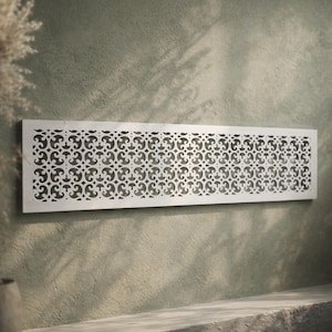 Op de afbeelding: Een rechthoekig, zilverkleurig decoratief wandpaneel met een herhaald, opengewerkt patroon van wervelende vormen. Het paneel is gemonteerd op een getextureerde, olijfgroene muur, waardoor een contrast van texturen en kleuren ontstaat. Het ontwerp voegt elegantie toe.